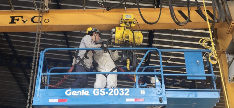 Técnicos con arnés inspeccionando el polipasto de una grúa puente desde una plataforma