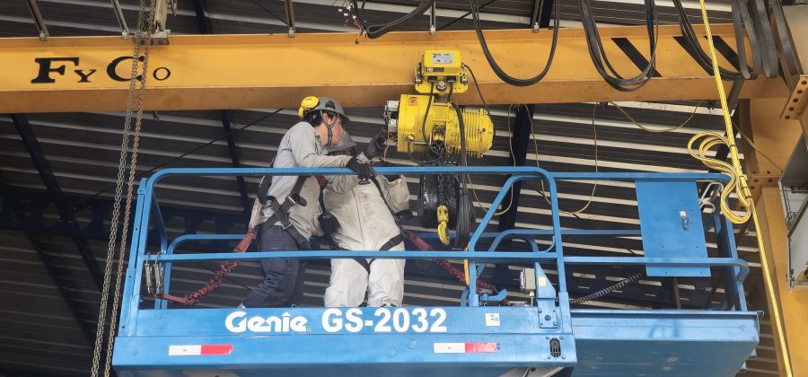 Técnicos con arnés inspeccionando el polipasto de una grúa puente desde una plataforma
