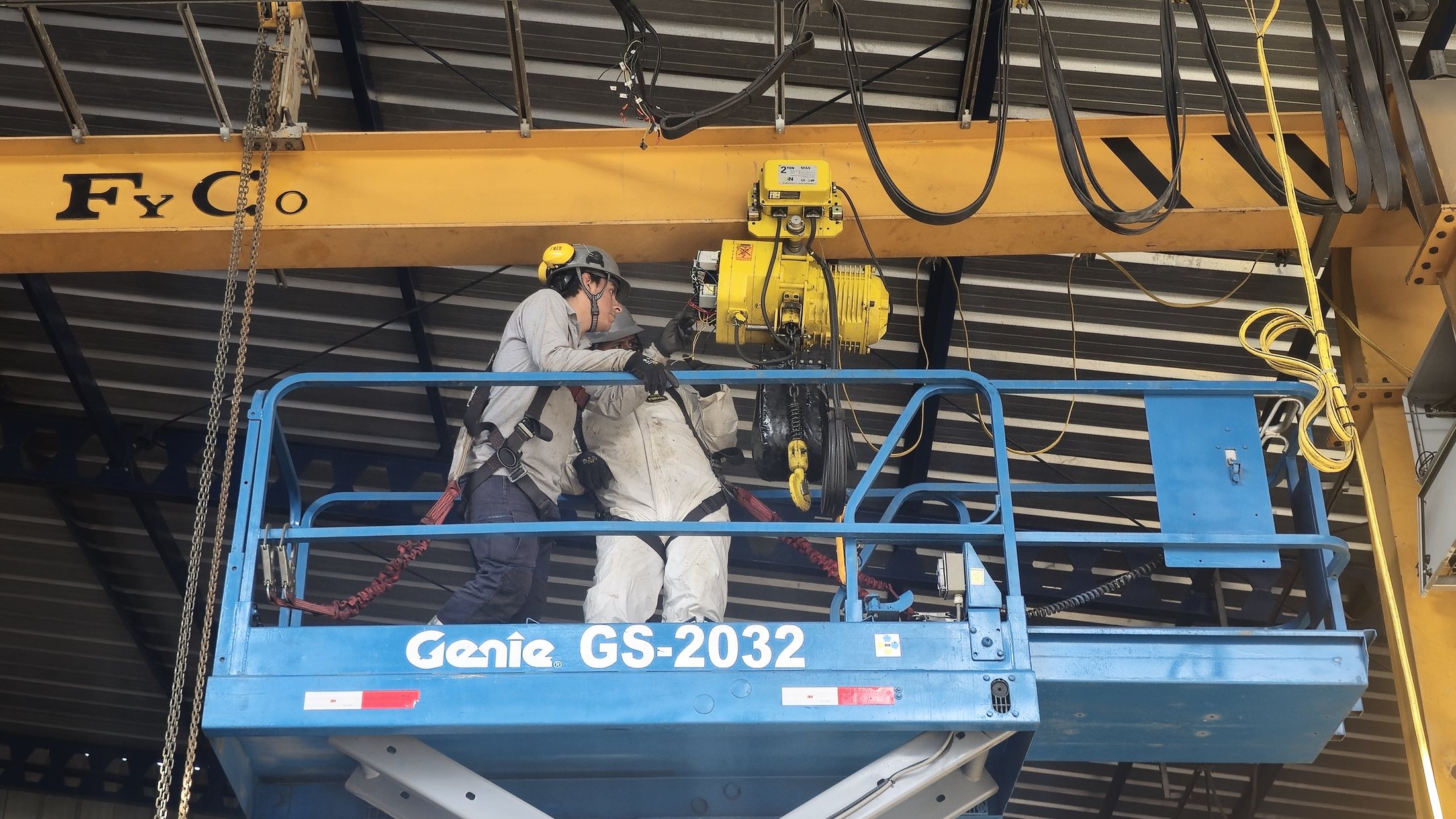Técnicos con arnés inspeccionando el polipasto de una grúa puente desde una plataforma
